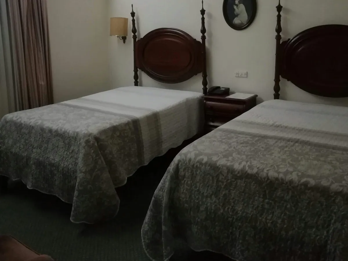 Phòng twin hồ Lắk: hai giường đơn trải ga hoa văn xám, đầu giường gỗ và bàn đầu giường ở giữa
